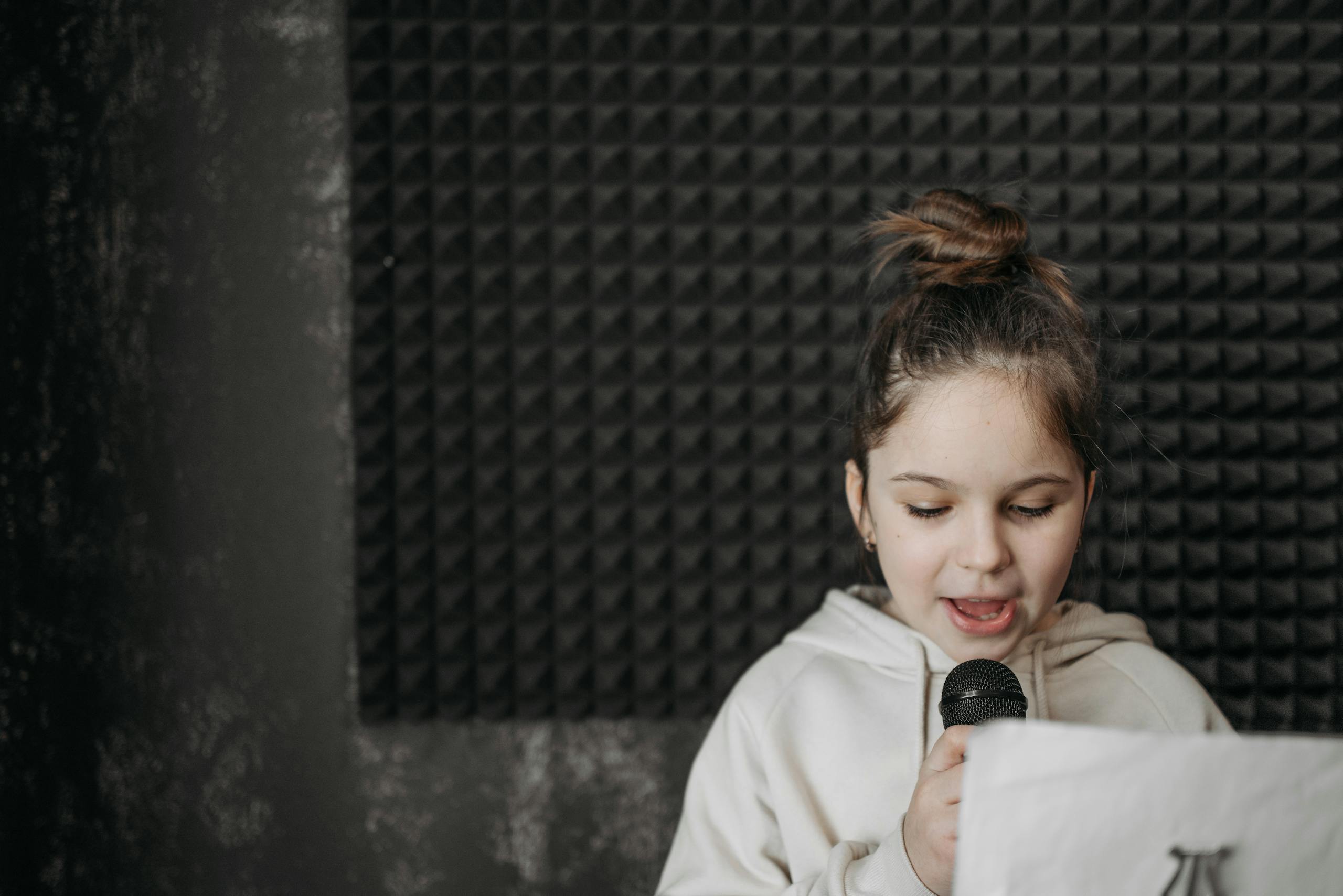 A young girl singing into a microphone in a soundproof recording studio.