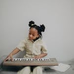 A young girl with dreadlocks playing an electronic keyboard on a gray sofa, creating a serene and minimalistic scene.